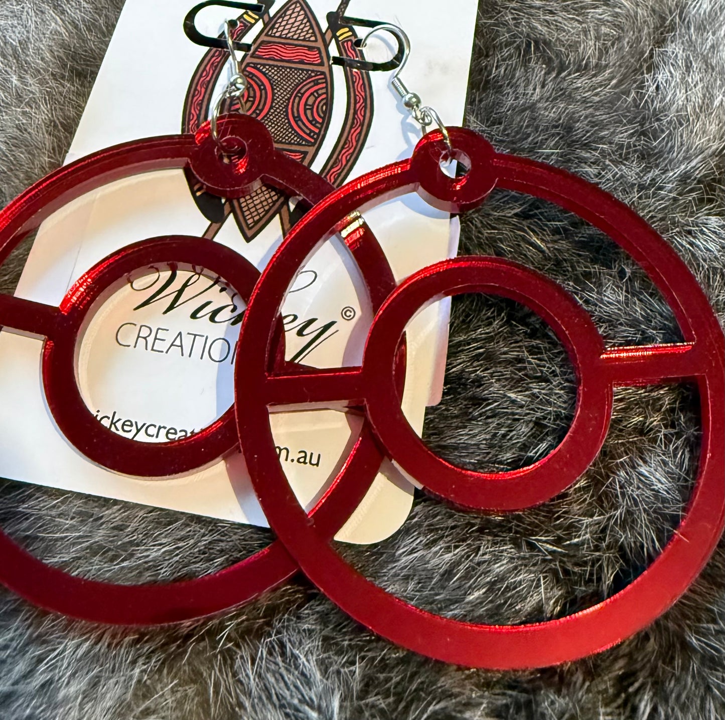 Red hoop earrings on a furry surface with a visible brand label.
