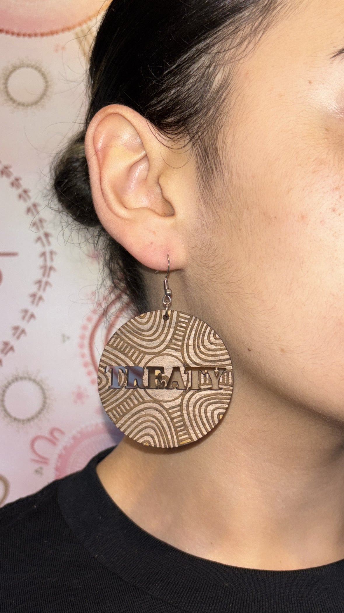 Person wearing a gold circular earring with 'DREAM' engraved on it, against a blurred background.