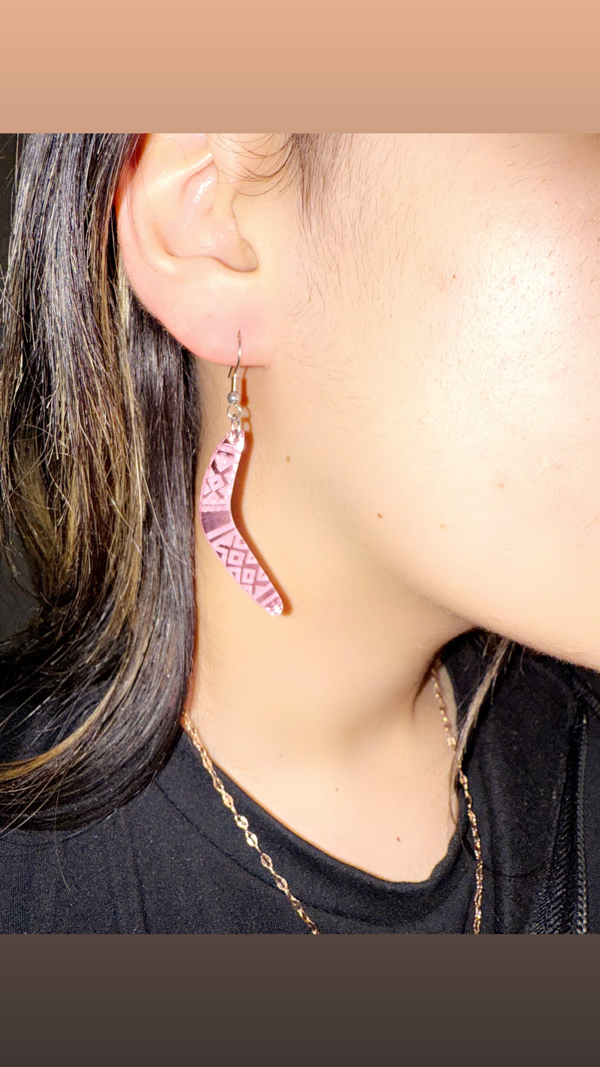 Close-up of a person wearing pink geometric earrings with a neutral background