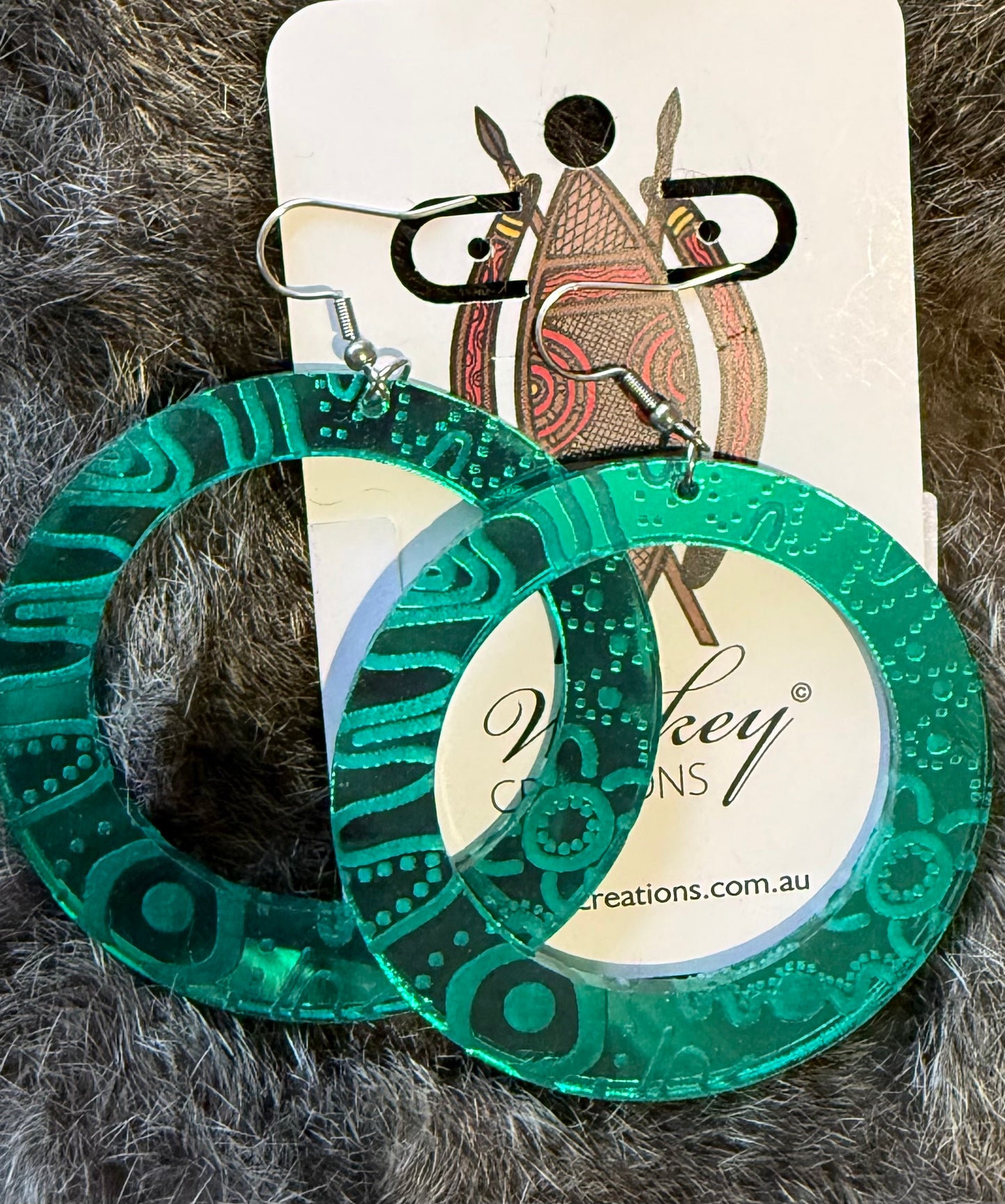 Green patterned hoop earrings on a gray textured surface with a visible brand label.