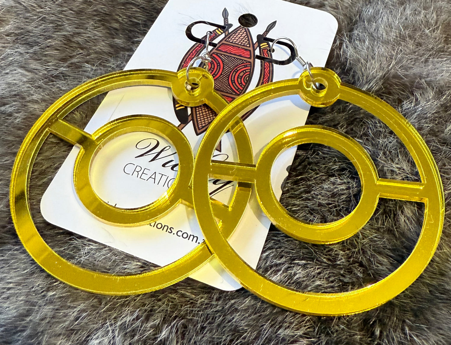 Gold circular earrings on a fur surface with a visible brand card.