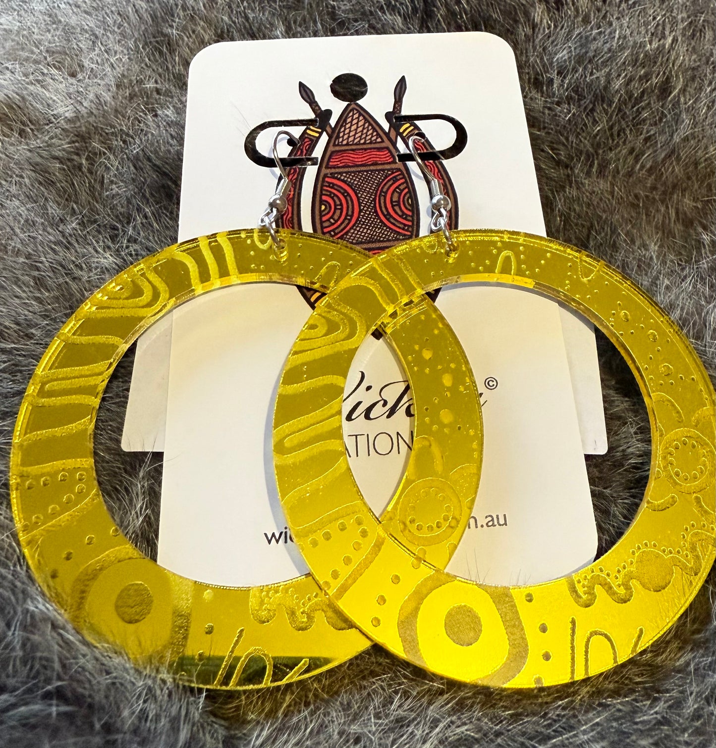 Gold hoop earrings on a white card with visible branding, placed on a textured gray surface.