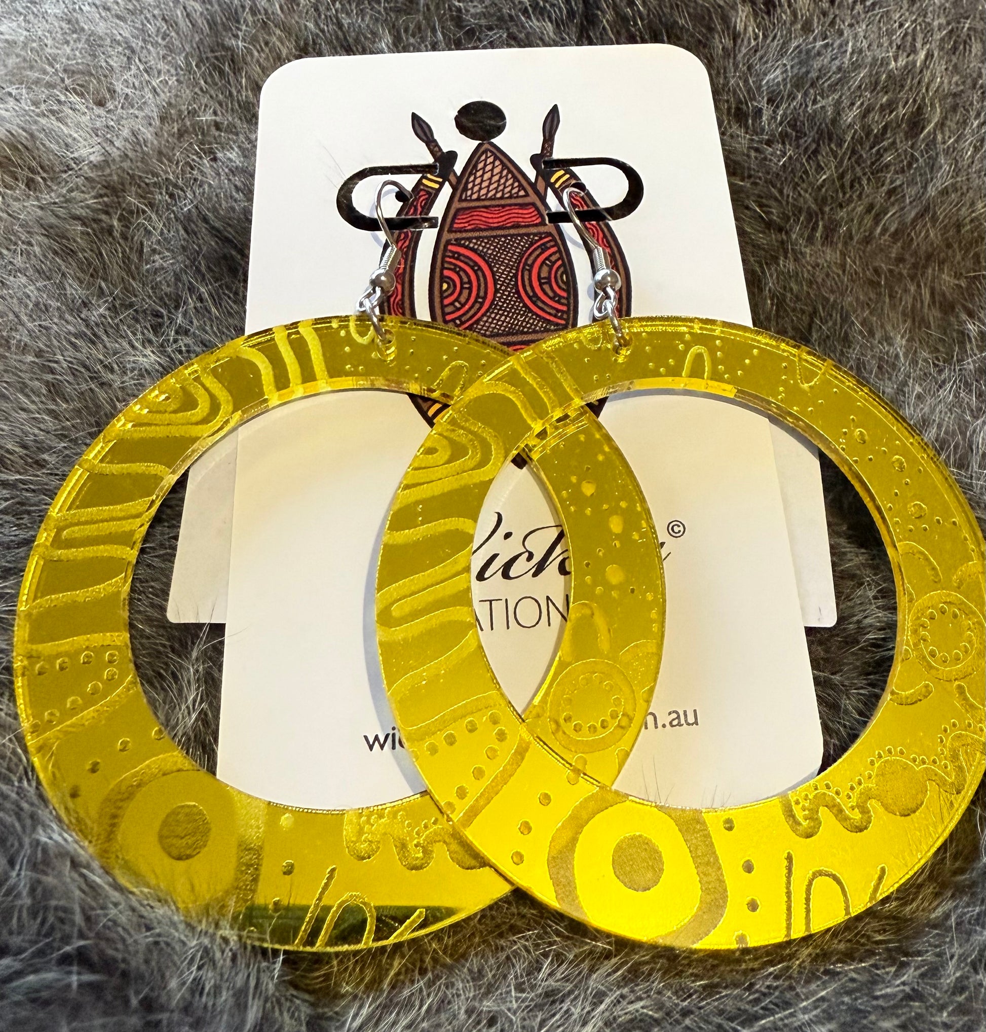 Gold hoop earrings on a white card with visible branding, placed on a textured gray surface.